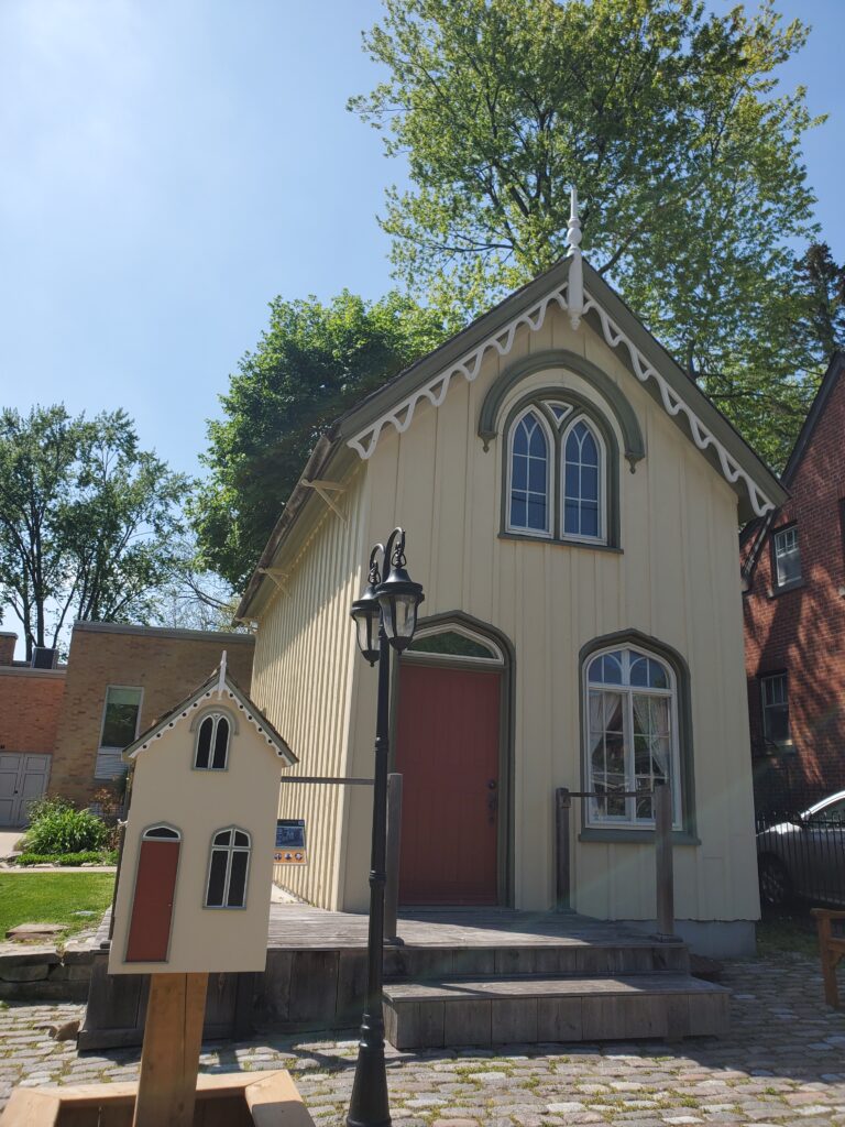 Image of the 1848 Doctor's Office, now painted yellow with a red door. A smaller version of the building  stand in front - a little library. 